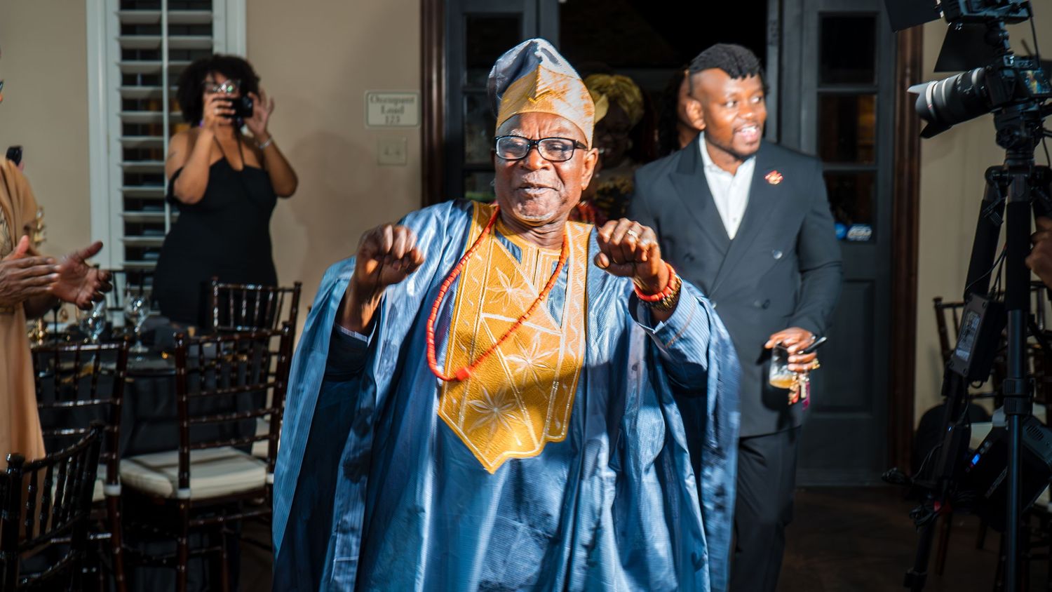 Man in traditional blue and gold attire dancing at an indoor birthday celebration