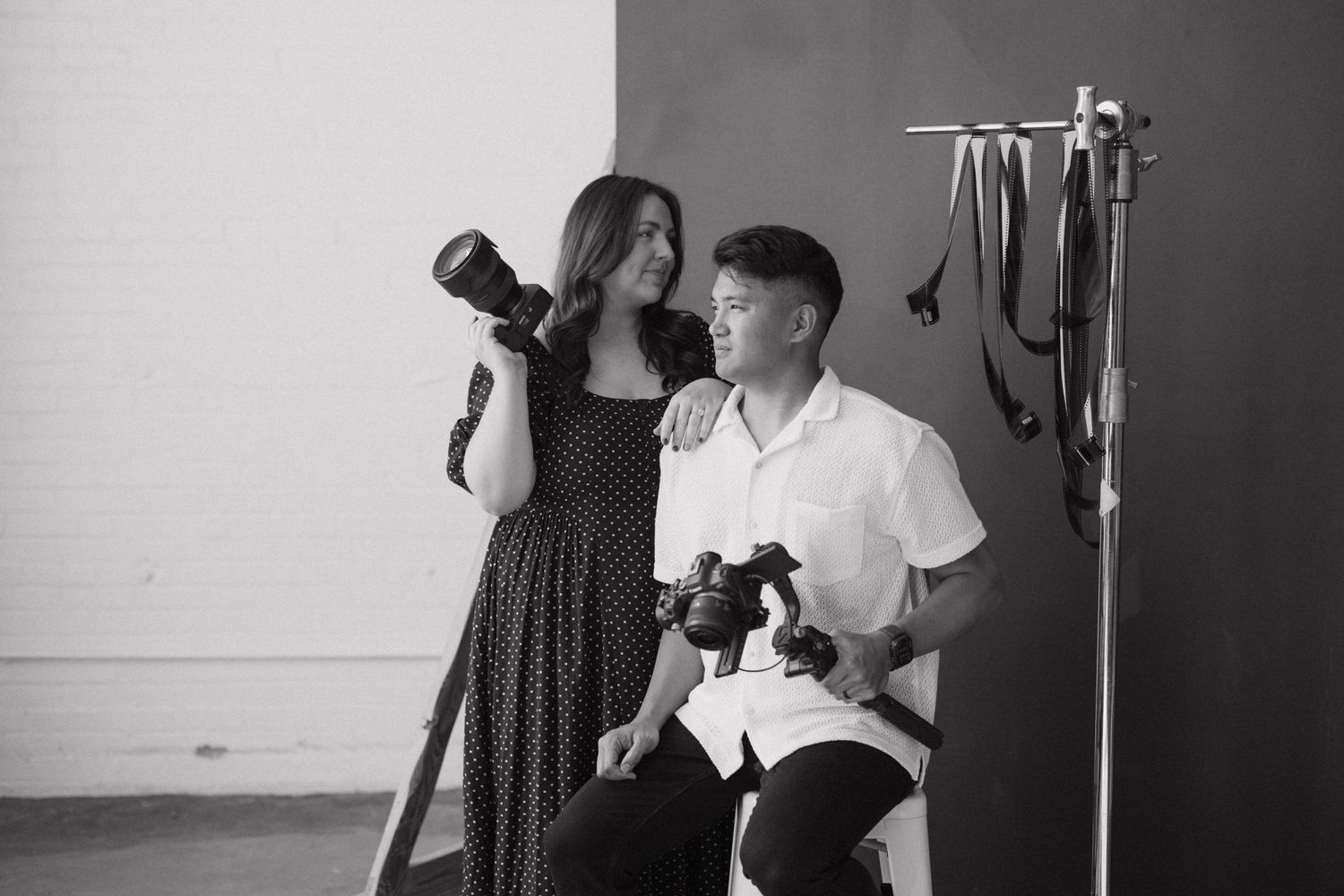 Black and white photo of two photographers holding cameras together in a studio setting.