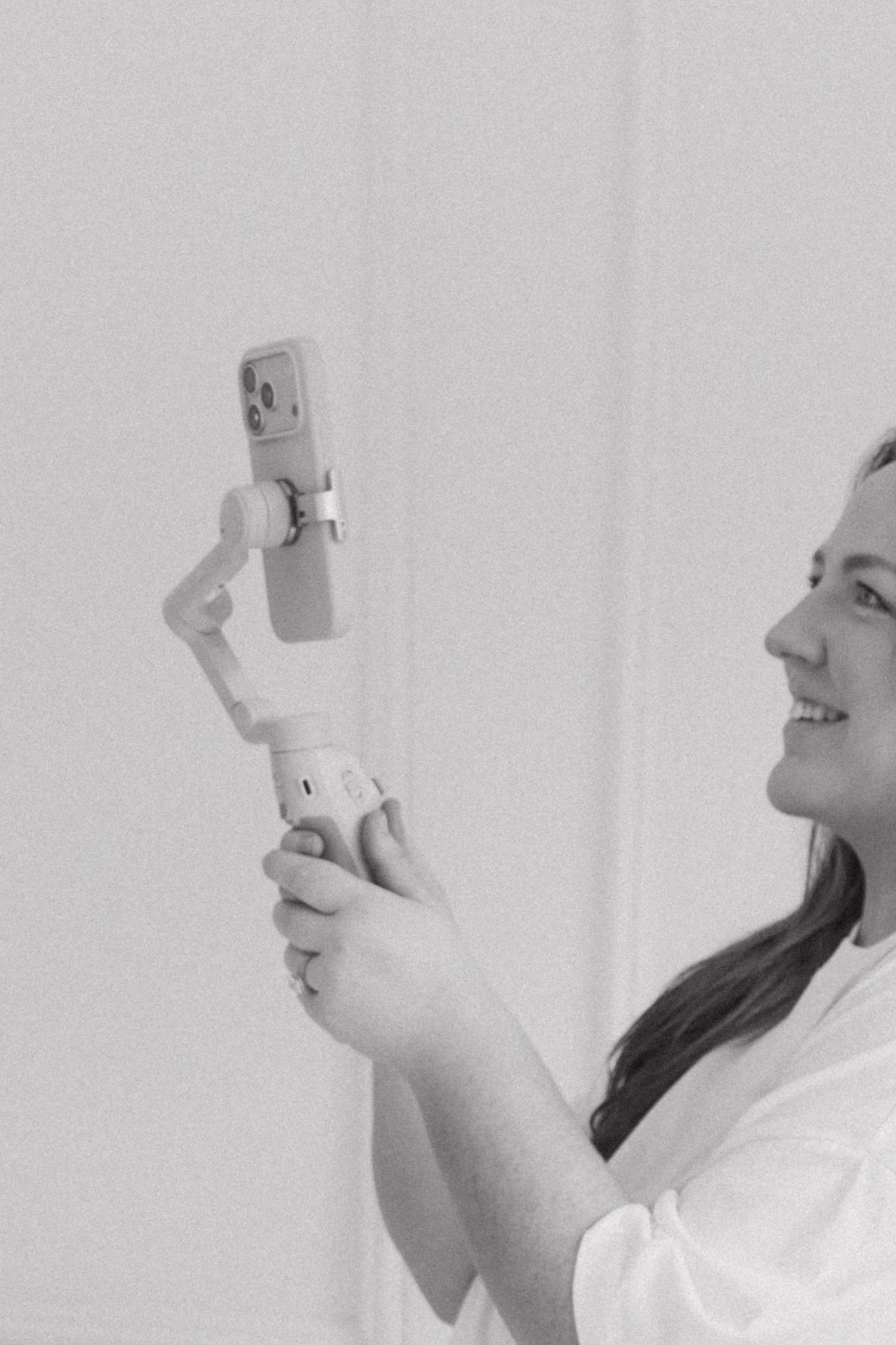 Woman smiling while holding a smartphone gimbal stabilizer, captured in black and white photography.