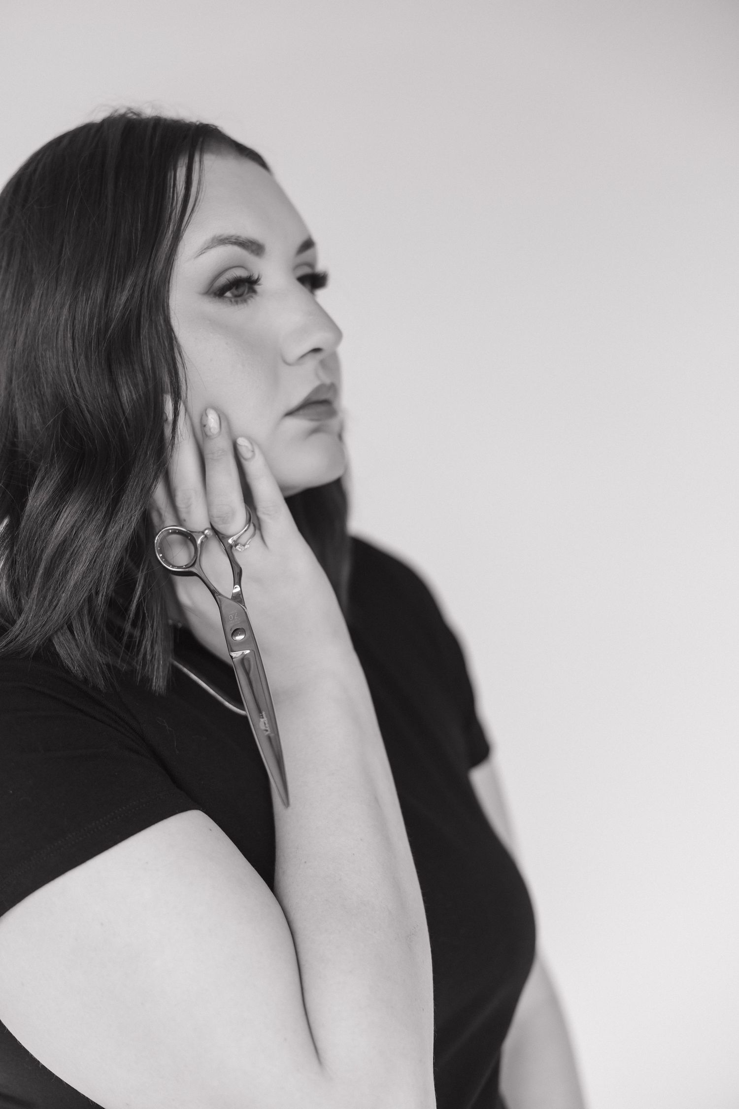 Black and white portrait of a woman holding scissors near her face in a professional studio.