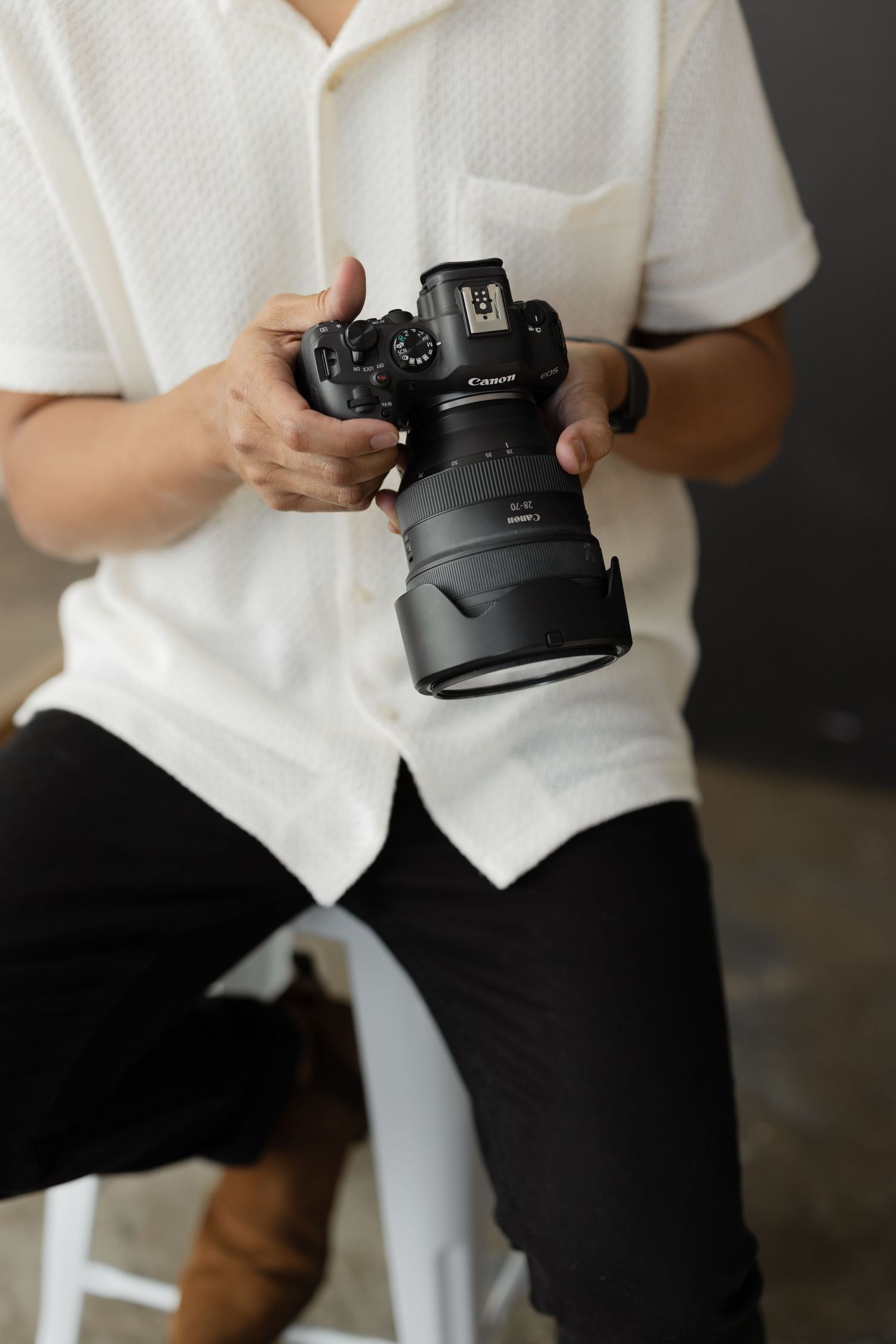 Person in white shirt holding a Canon DSLR camera with large lens in a photography studio.