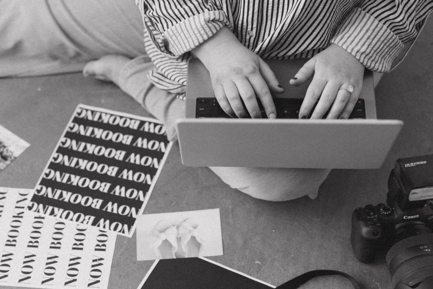 Overhead black and white view of hands typing on laptop surrounded by booking flyers.