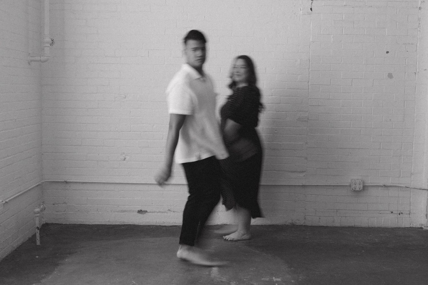 Black and white photo of man and woman walking together in minimalist white room.