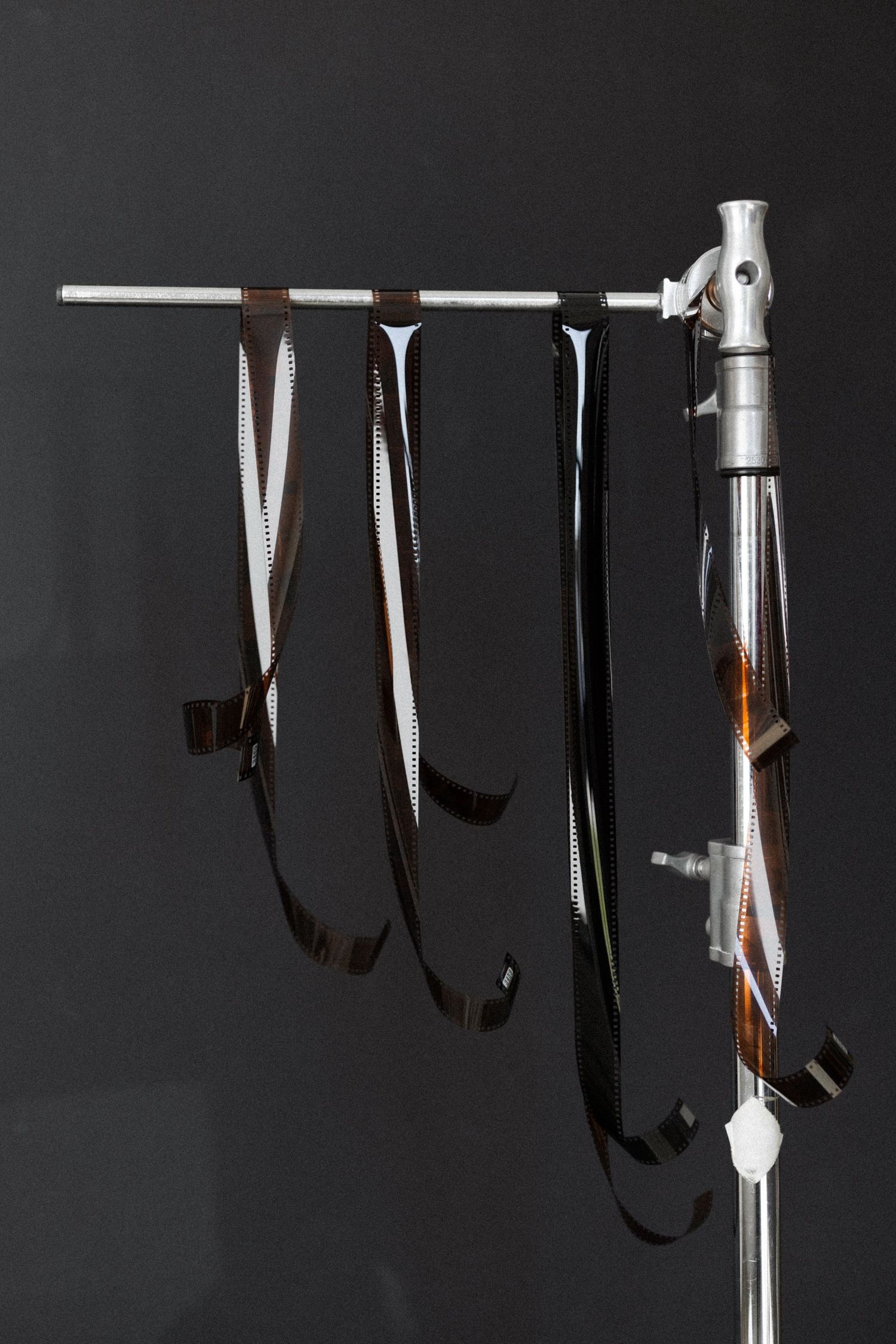 Strips of developed photographic film hanging from a metal stand against a dark gray background.