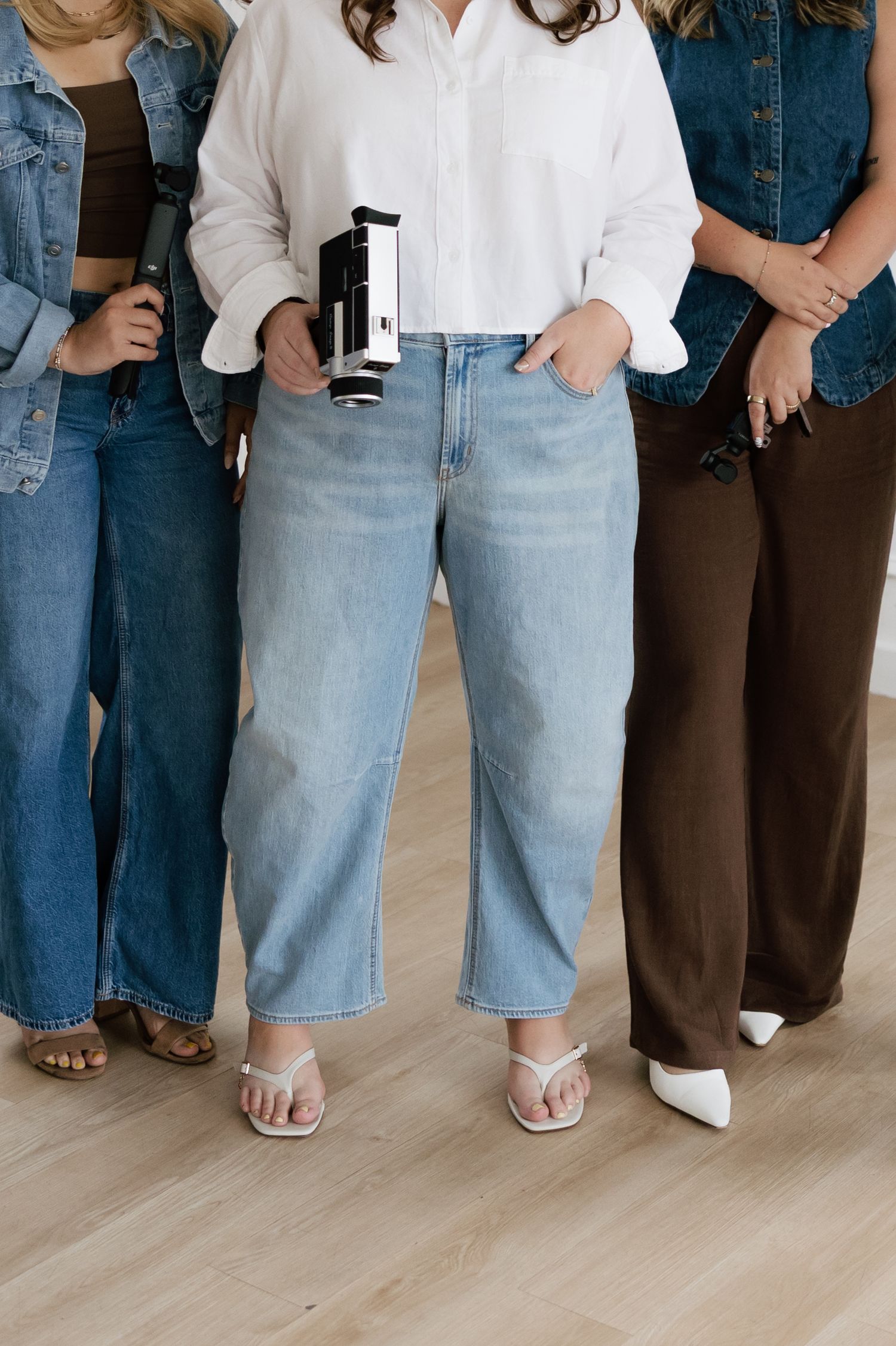 Four women wearing wide-leg jeans and casual tops, styled with white sandals and heels on a light wood floor.