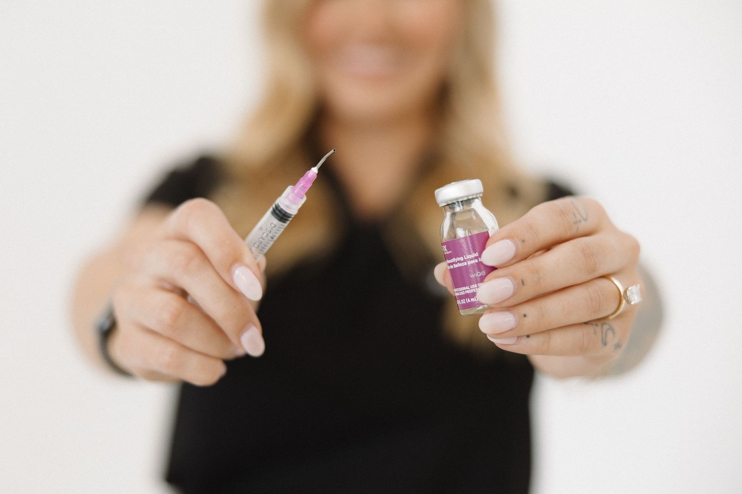 Woman holding a medical syringe and pink vial vaccine bottle in both hands against white background.