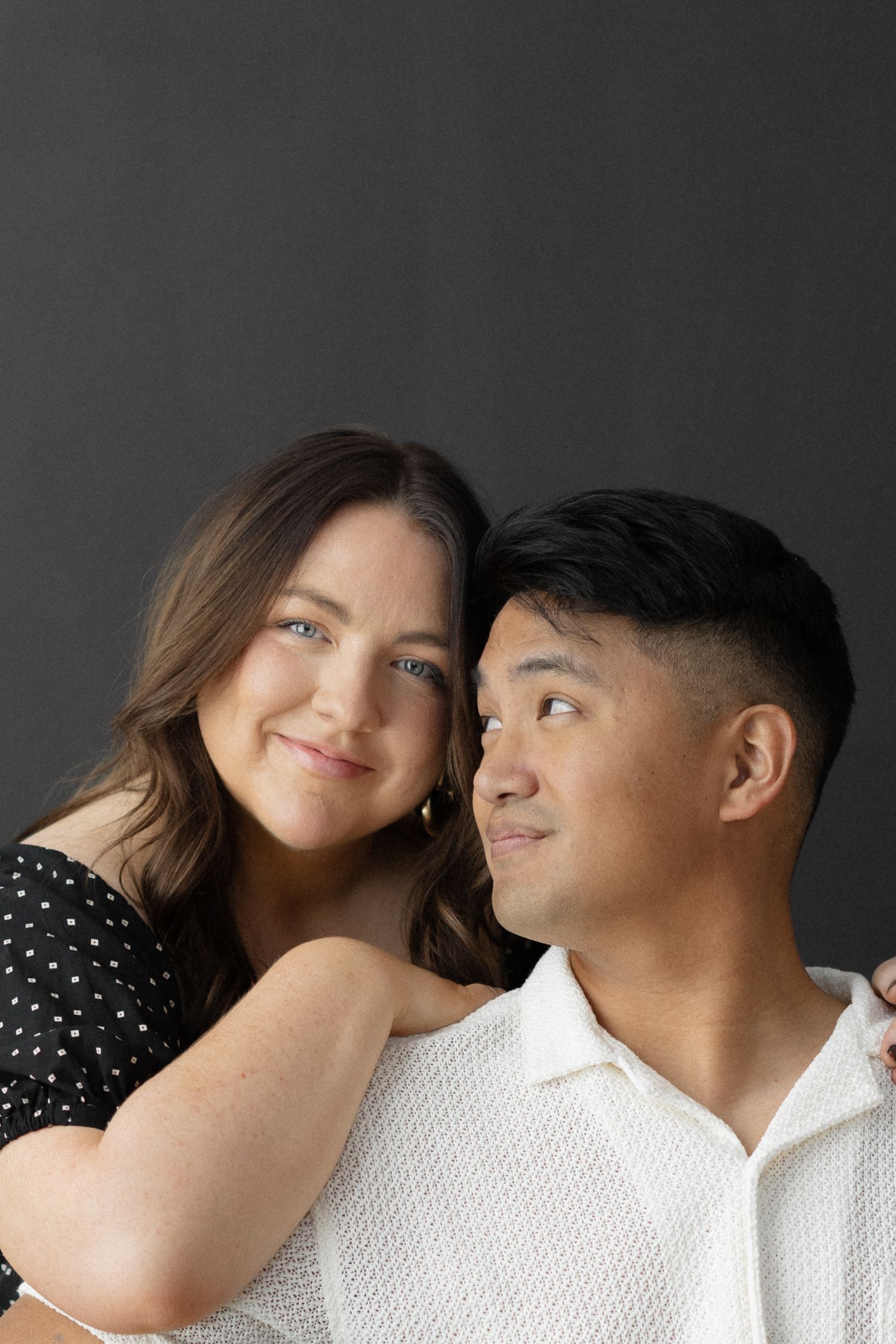 Smiling couple posing together against dark gray background in a professional portrait studio.