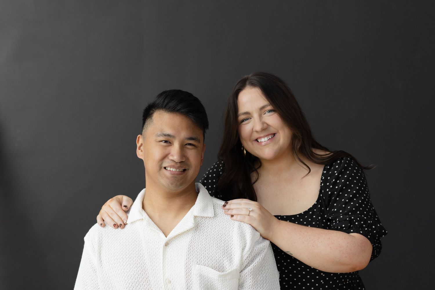 Smiling man and woman posing together against a dark gray studio background.