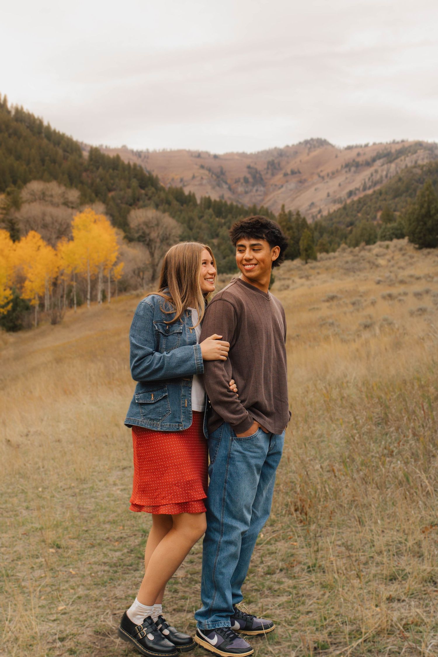 Young couple embracing in autumn mountain meadow with golden aspen trees and hills in background.