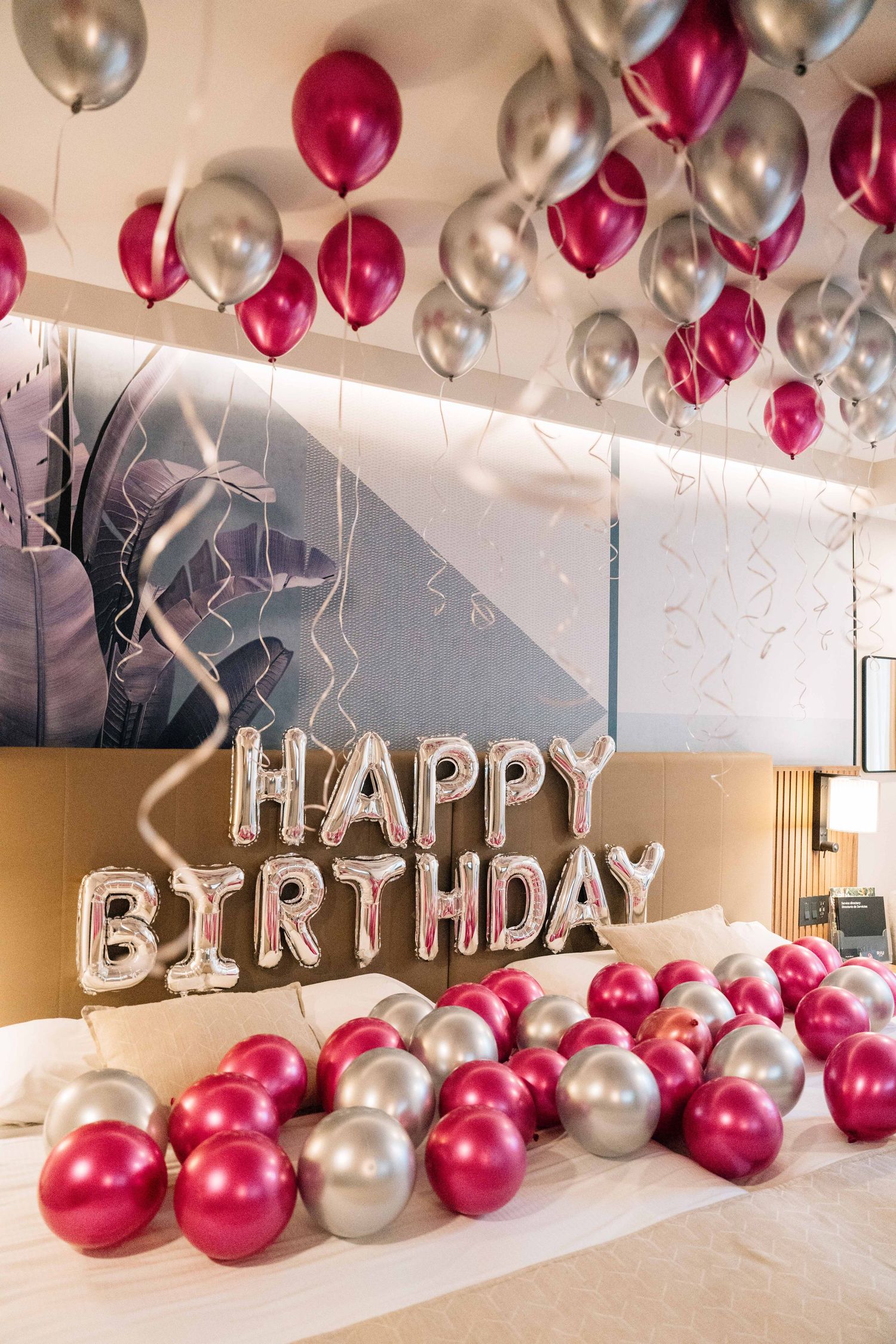 Silver and burgundy balloons decorate a room with 'Happy Birthday' text spelled out in metallic letter balloons.