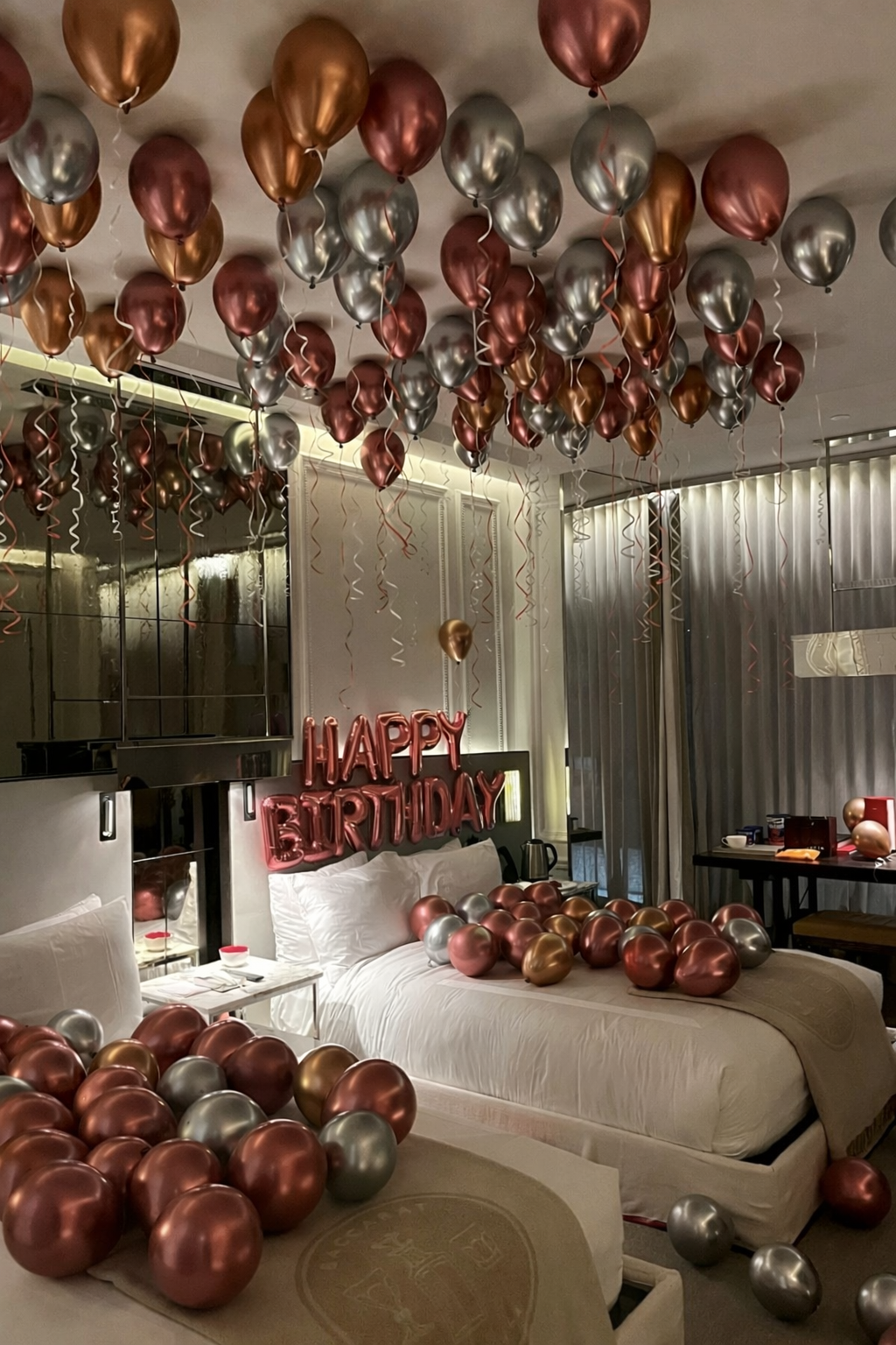 Luxurious party room decorated with metallic rose gold and silver balloons covering the ceiling with Happy Birthday text.