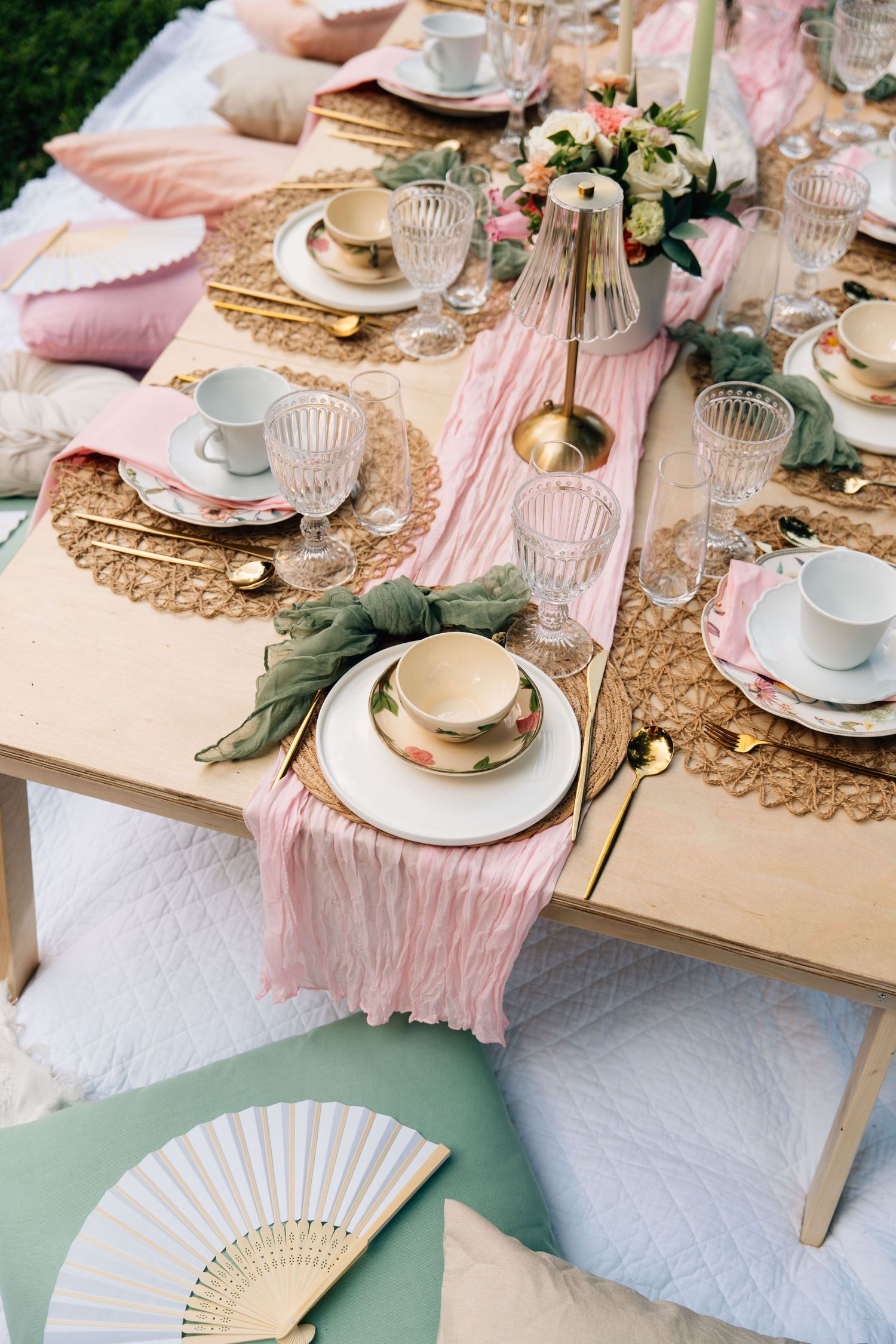 Elegant pink and gold table setting with vintage fans, floral accents, and delicate glassware for a romantic celebration.