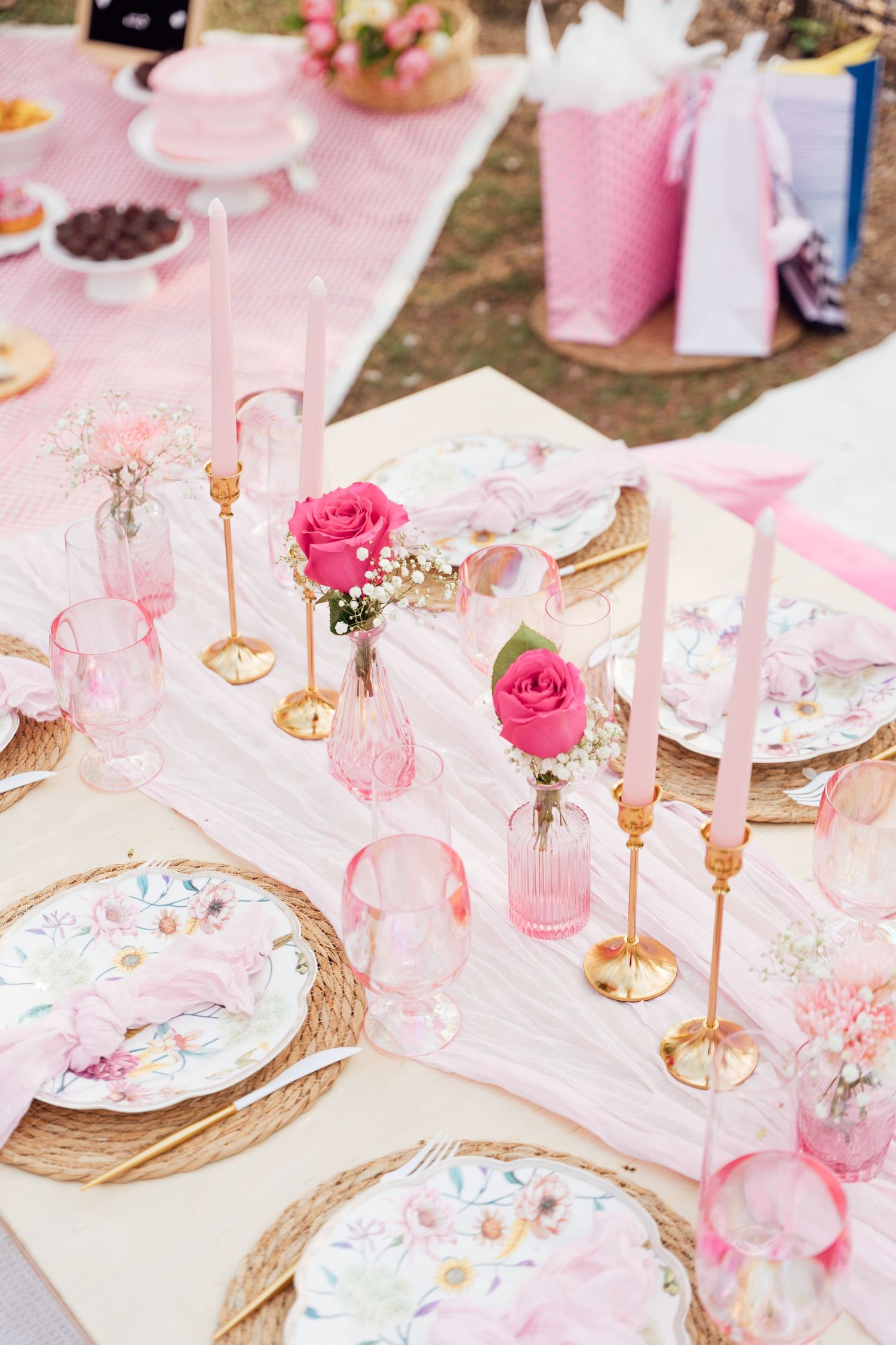 Elegant pink and white table setting with roses, gold candlesticks, and floral china plates for a romantic celebration.
