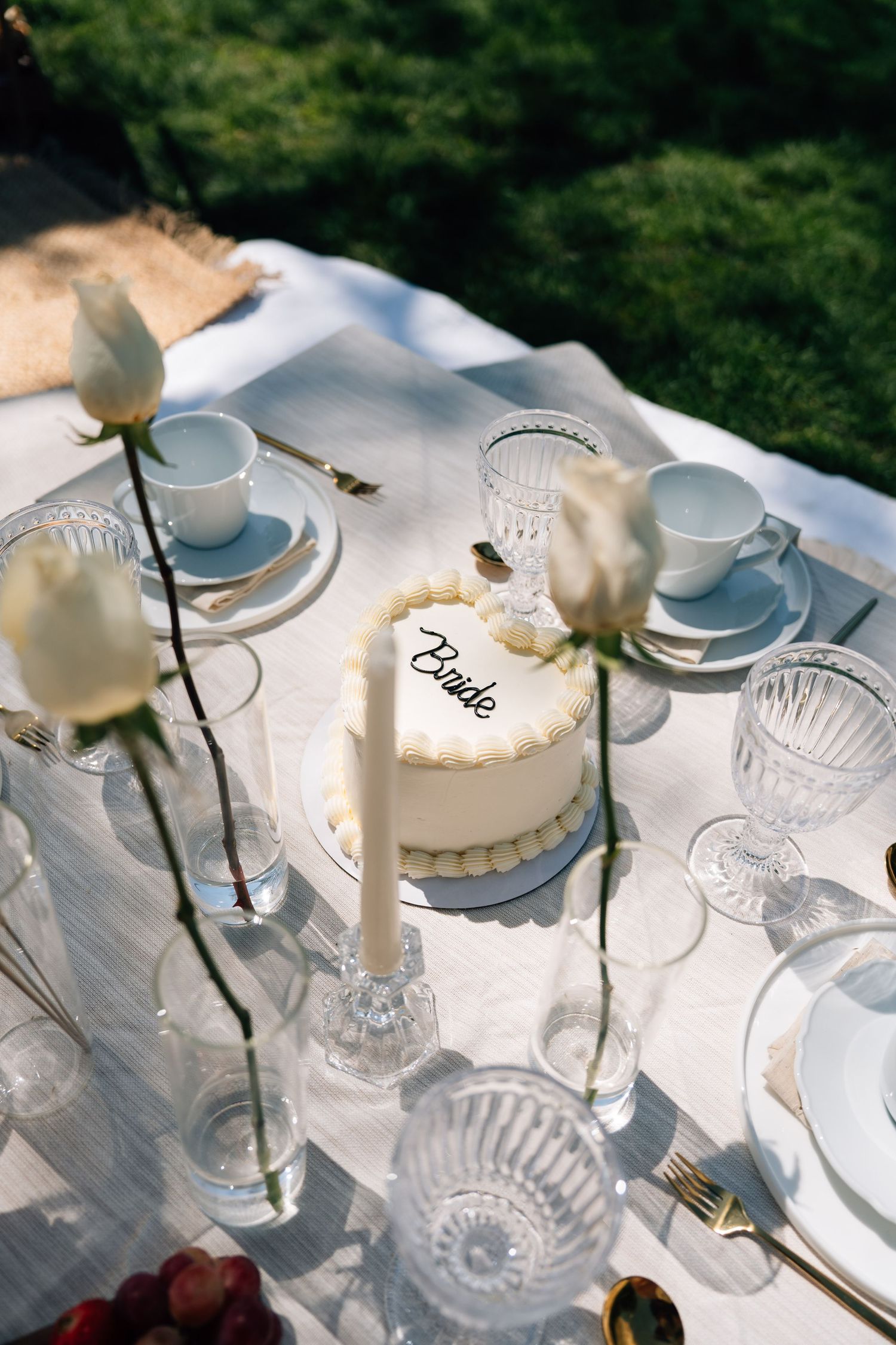 Elegant bridal table setting with heart-shaped bride cake, white roses, crystal glasses, and gold cutlery on linen tablecloth.