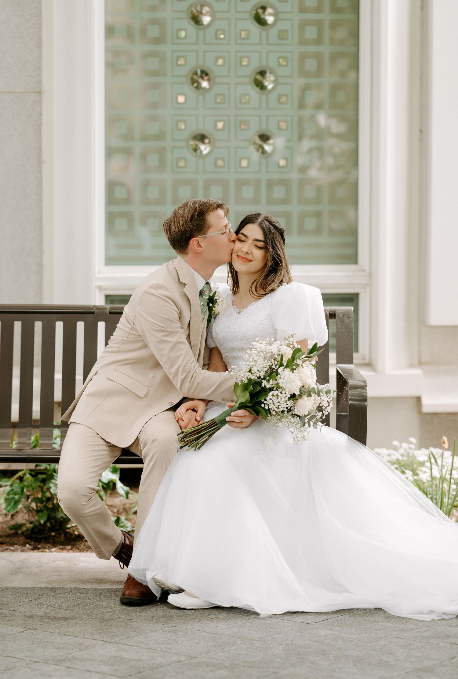 Groom kissing his bride while sitting on a bench at the Mt Timpanogos Utah Temple