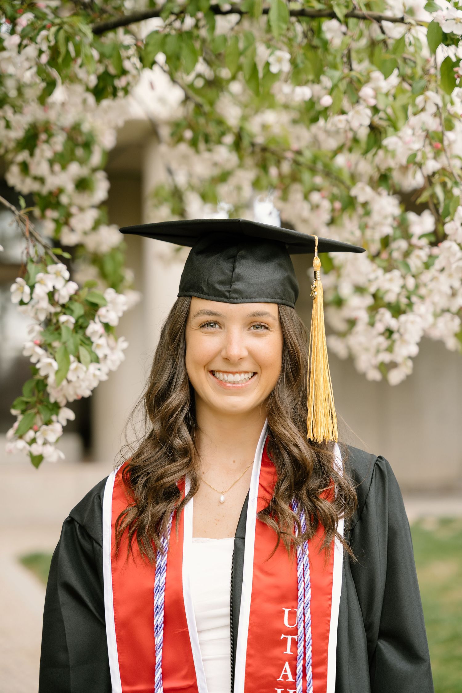 U of U graduate in front of a white cherry blossom tree in the Spring