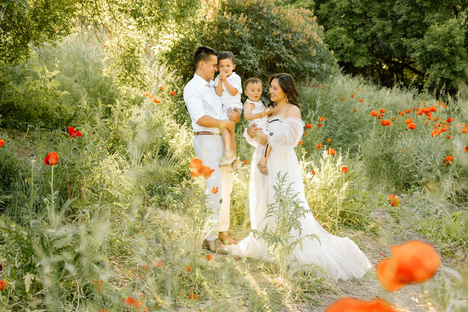 A family with 2 little boys in a field of poppies: the mom is wearing a cream ballgown