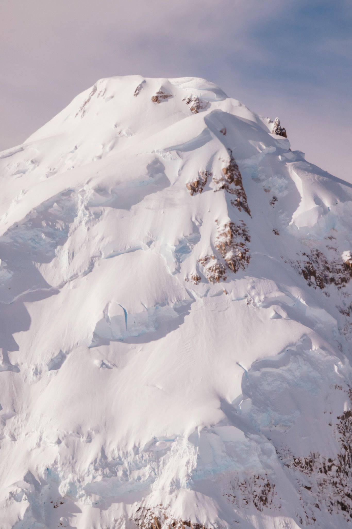 Stunning aerial view of snow-covered mountain peaks with rugged rock formations emerging through pristine white powder.