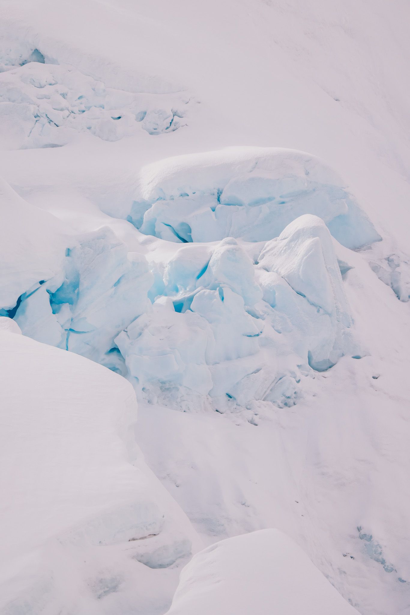 Close-up view of blue-tinted glacial ice formations with cracks and crevices in a snowy arctic landscape.
