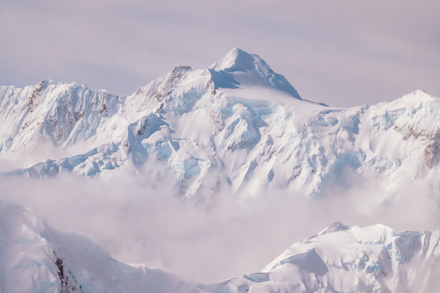 Snow-capped mountain peaks rise majestically against a bright sky in this panoramic winter landscape view.