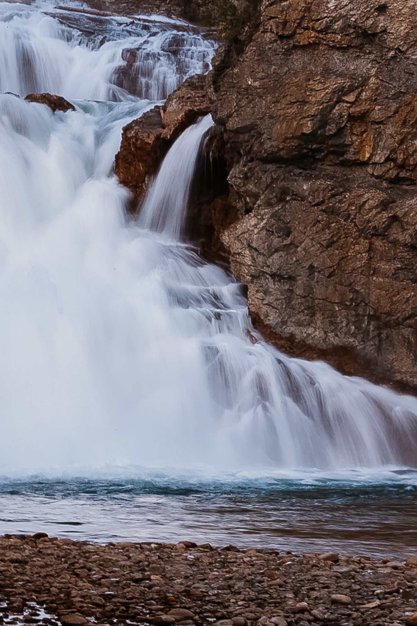 Powerful waterfall rushes over rocky cliff face creating white water spray.
