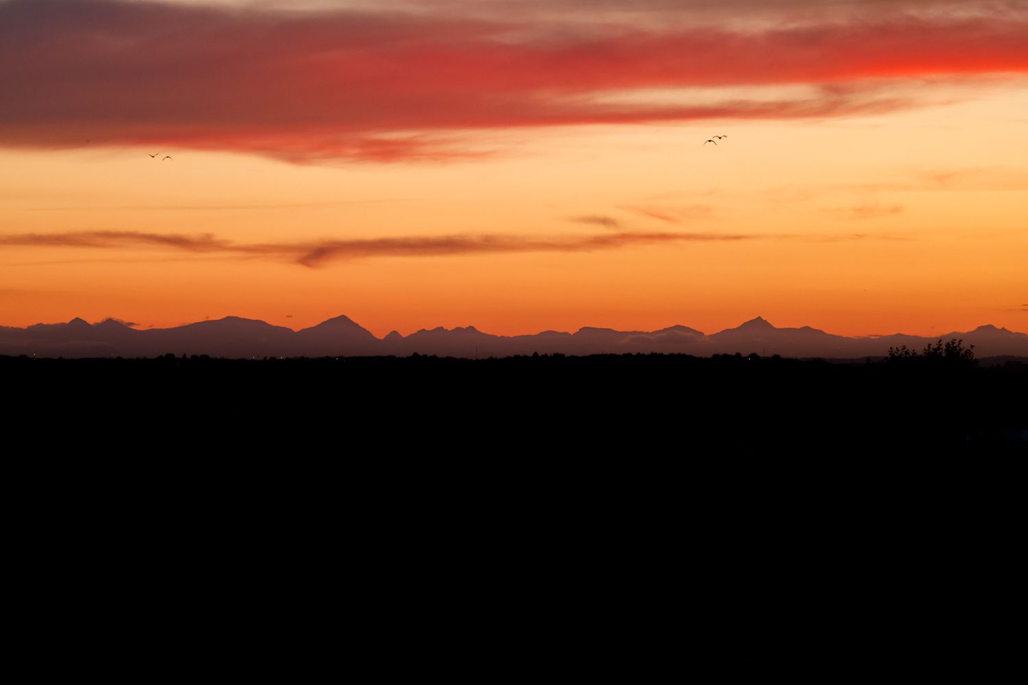 Mountain silhouettes stretch beneath a fiery orange sunset sky.