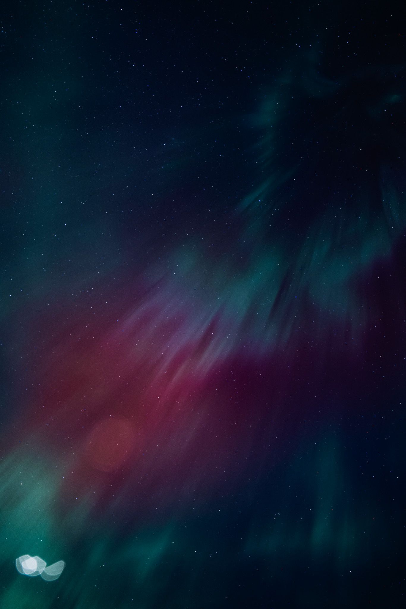 Colorful northern lights display featuring blending shades of turquoise, purple and red in the night sky.