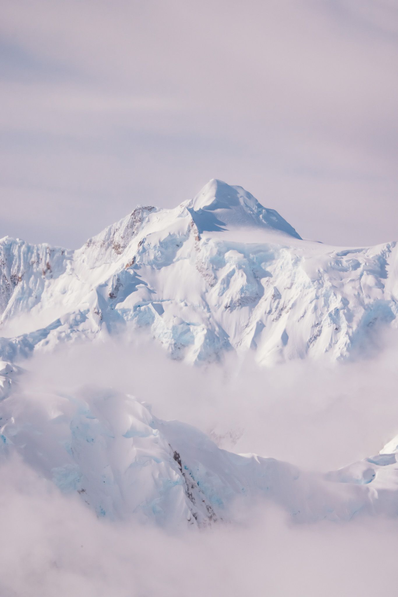 Snow-capped mountain peaks rise majestically above misty clouds in a panoramic winter landscape.