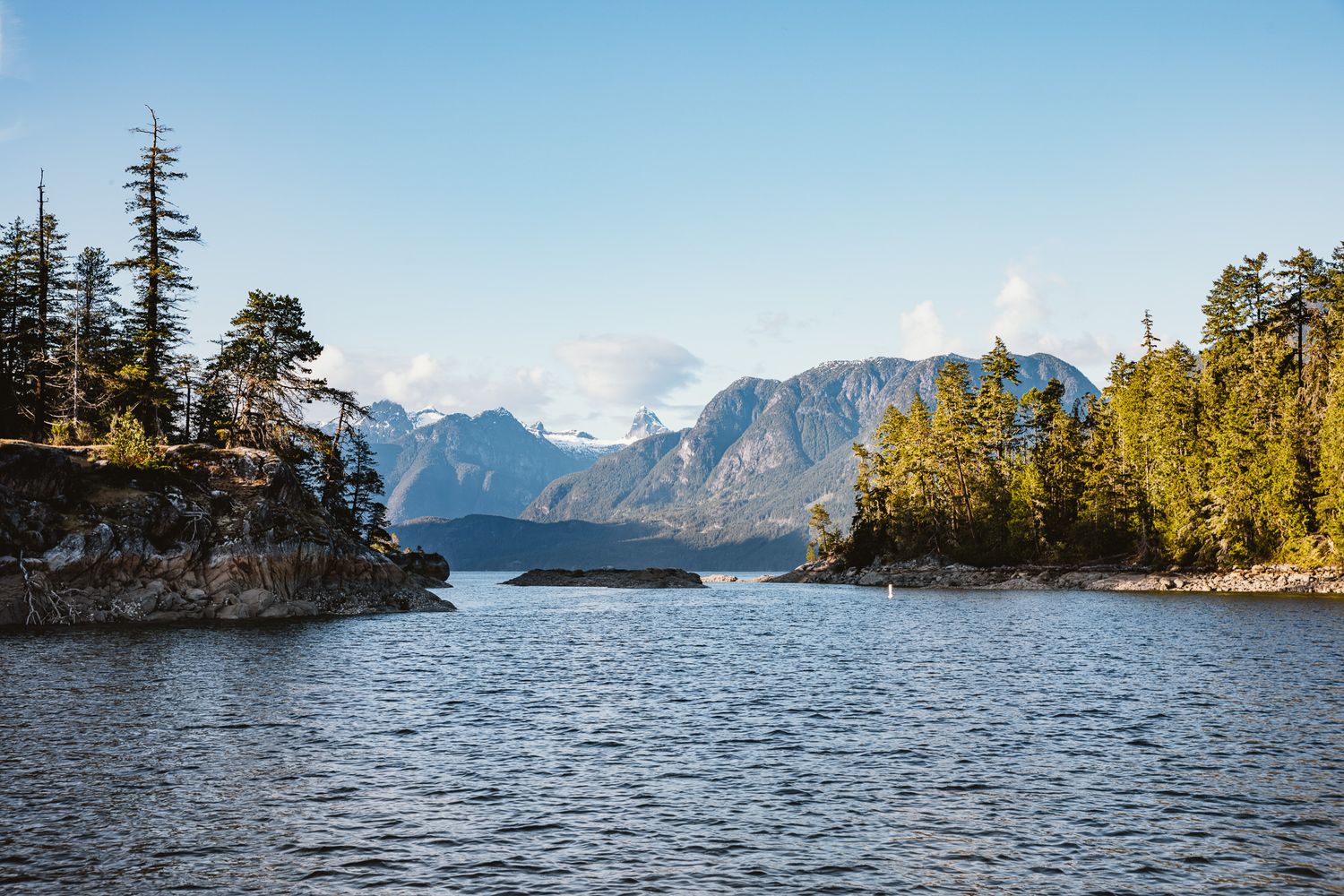 A scenic mountain lake surrounded by evergreen trees and rugged peaks under a blue sky.