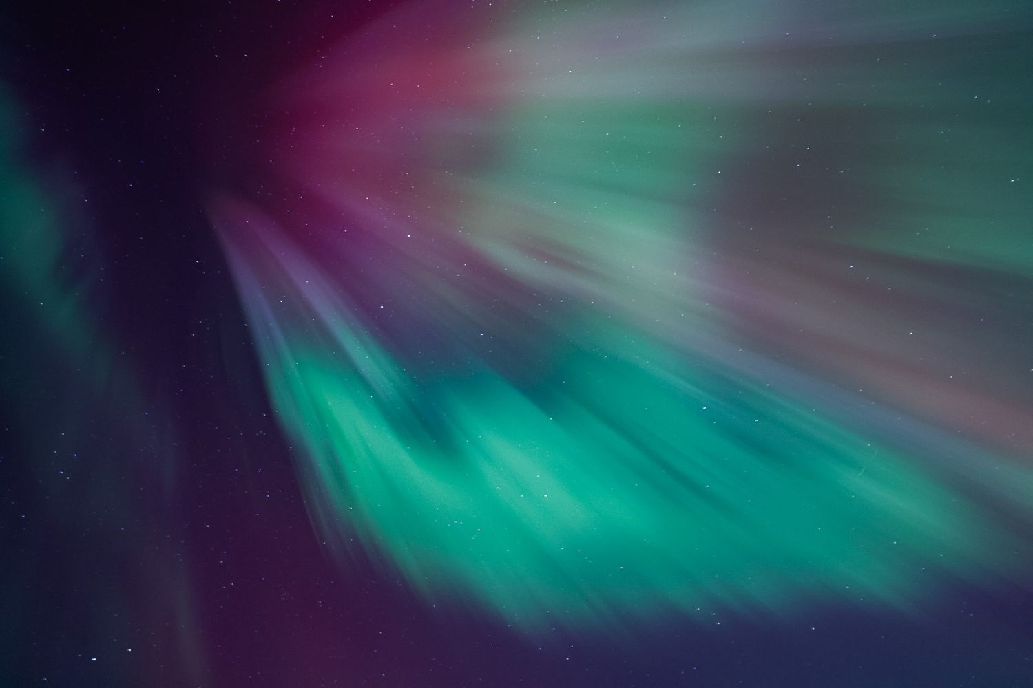 Vibrant aurora borealis displays swirling patterns of green and purple lights against the dark night sky.