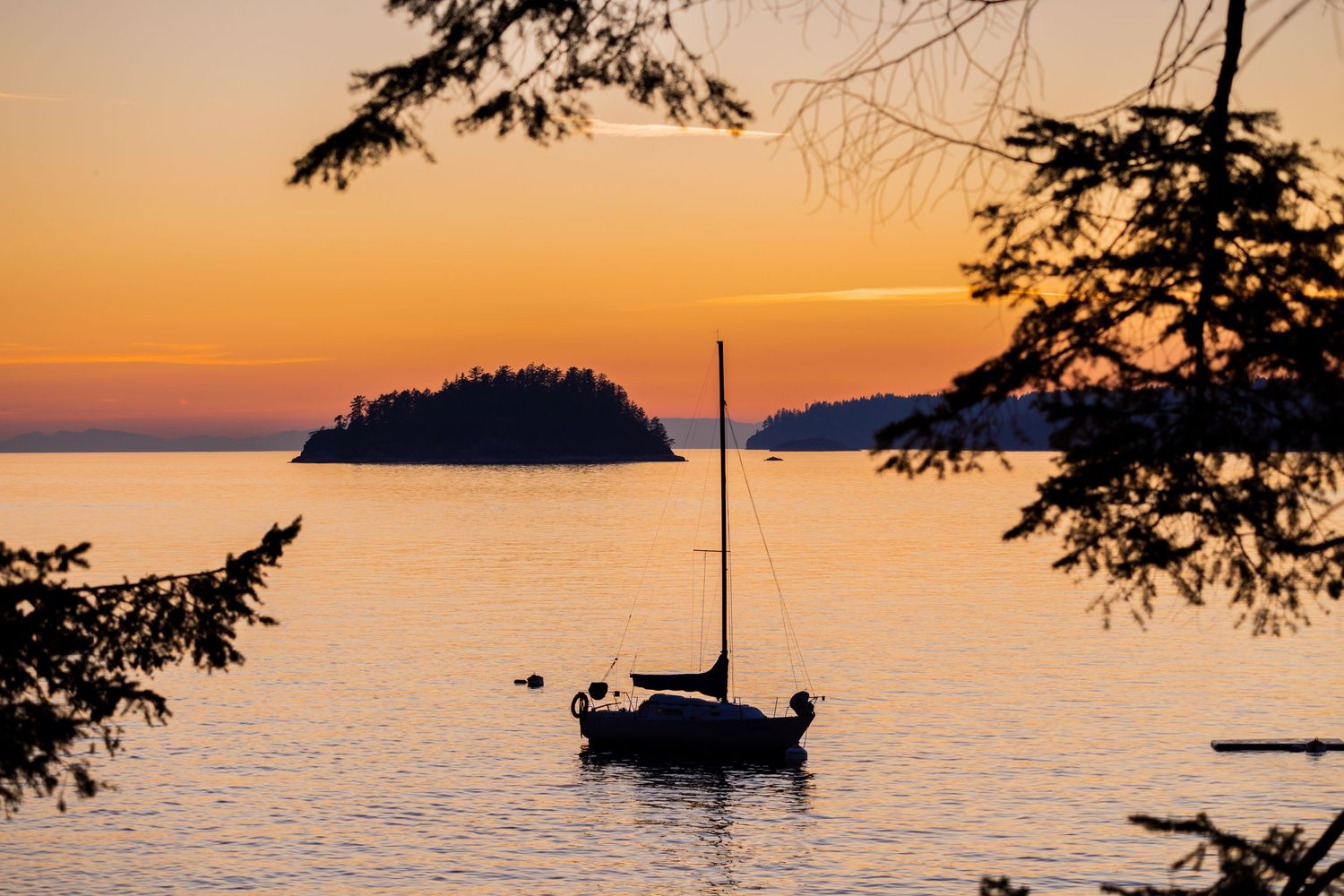 Sailboat silhouetted against a golden sunset over calm waters with islands in the distance.