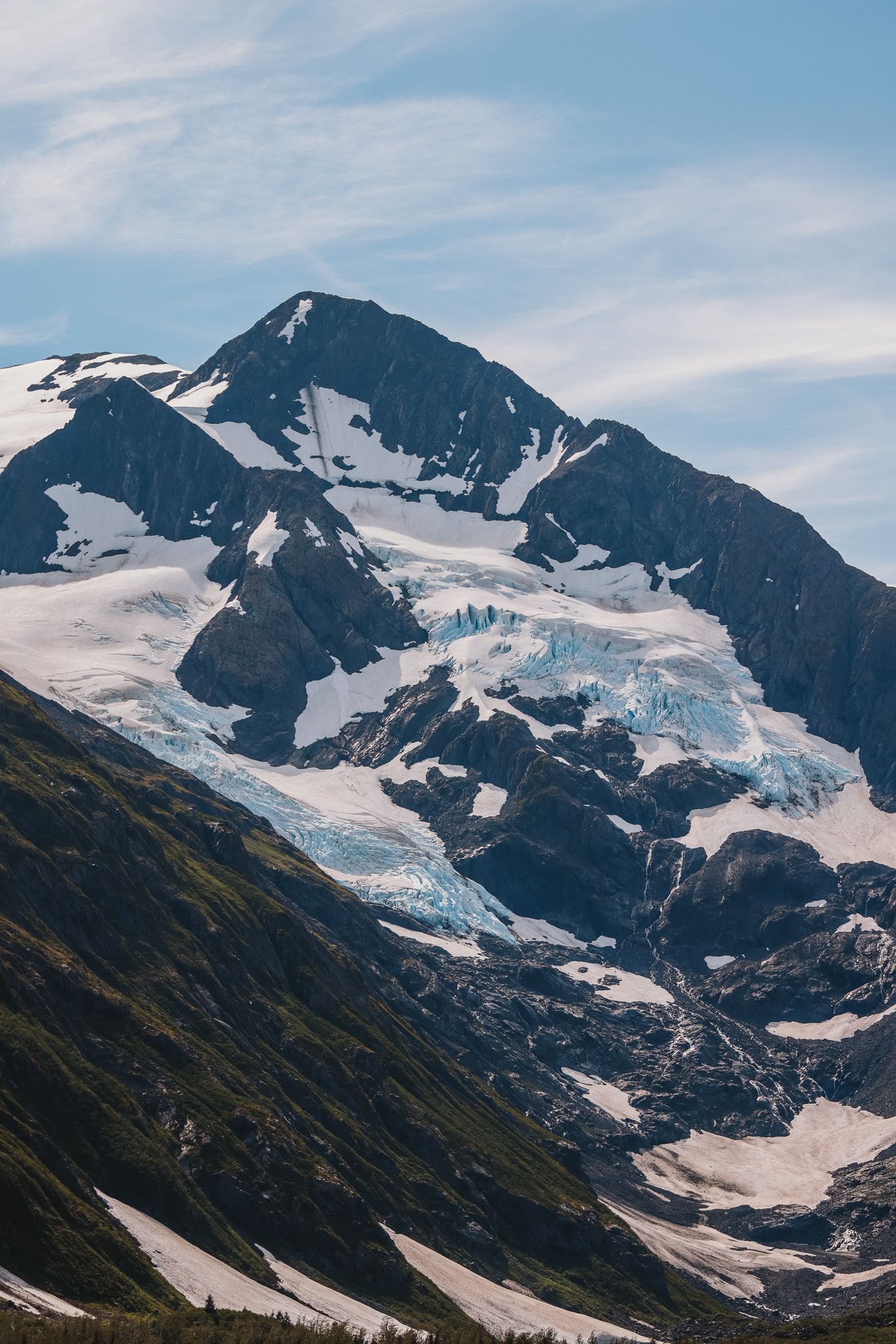 Massive glacier flows down steep mountain face with snow and ice formations.