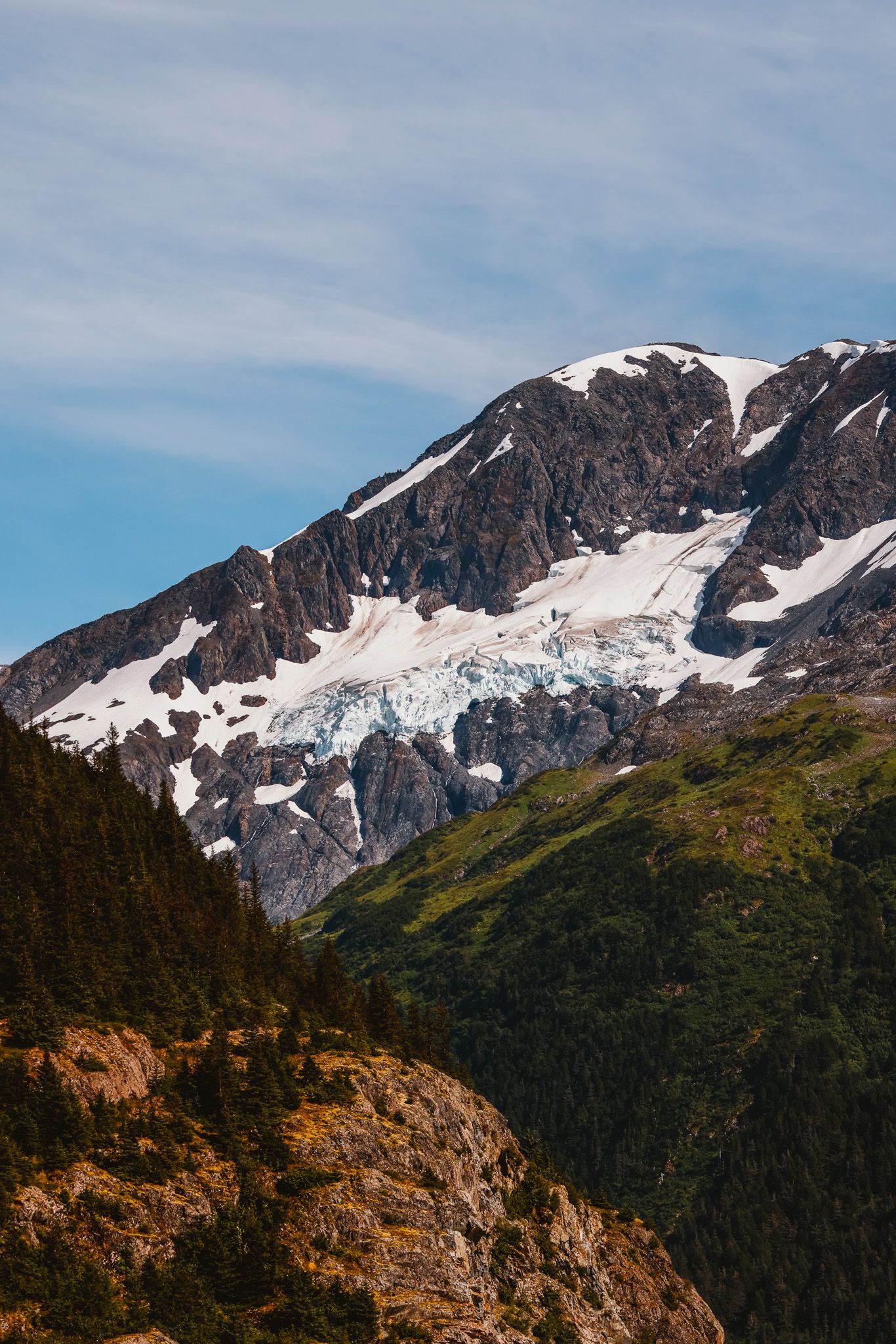 Snow-covered mountain peak with glaciers and rugged cliffs against bright blue sky.