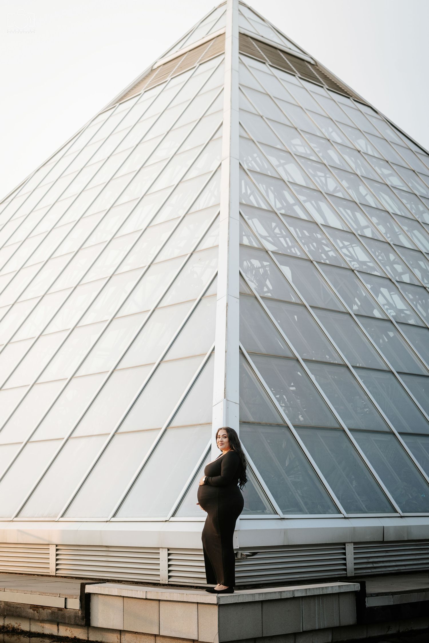 A modern architectural maternity photo against a geometric glass pyramid structure.