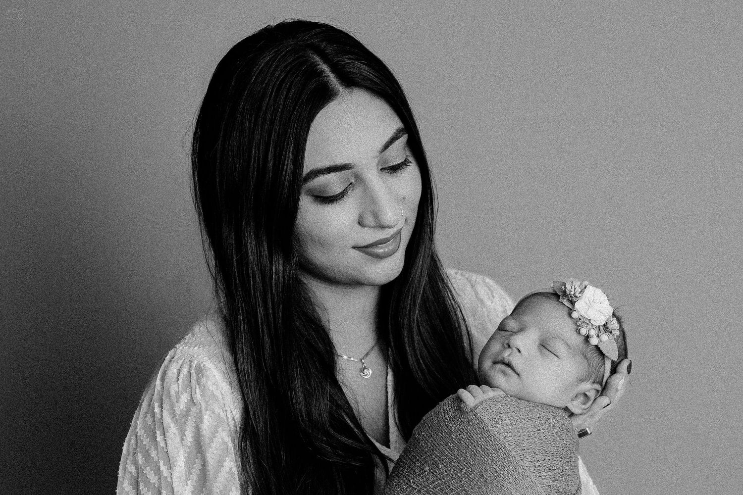 A tender black and white portrait of a mother cradling her newborn baby wrapped in swaddling.