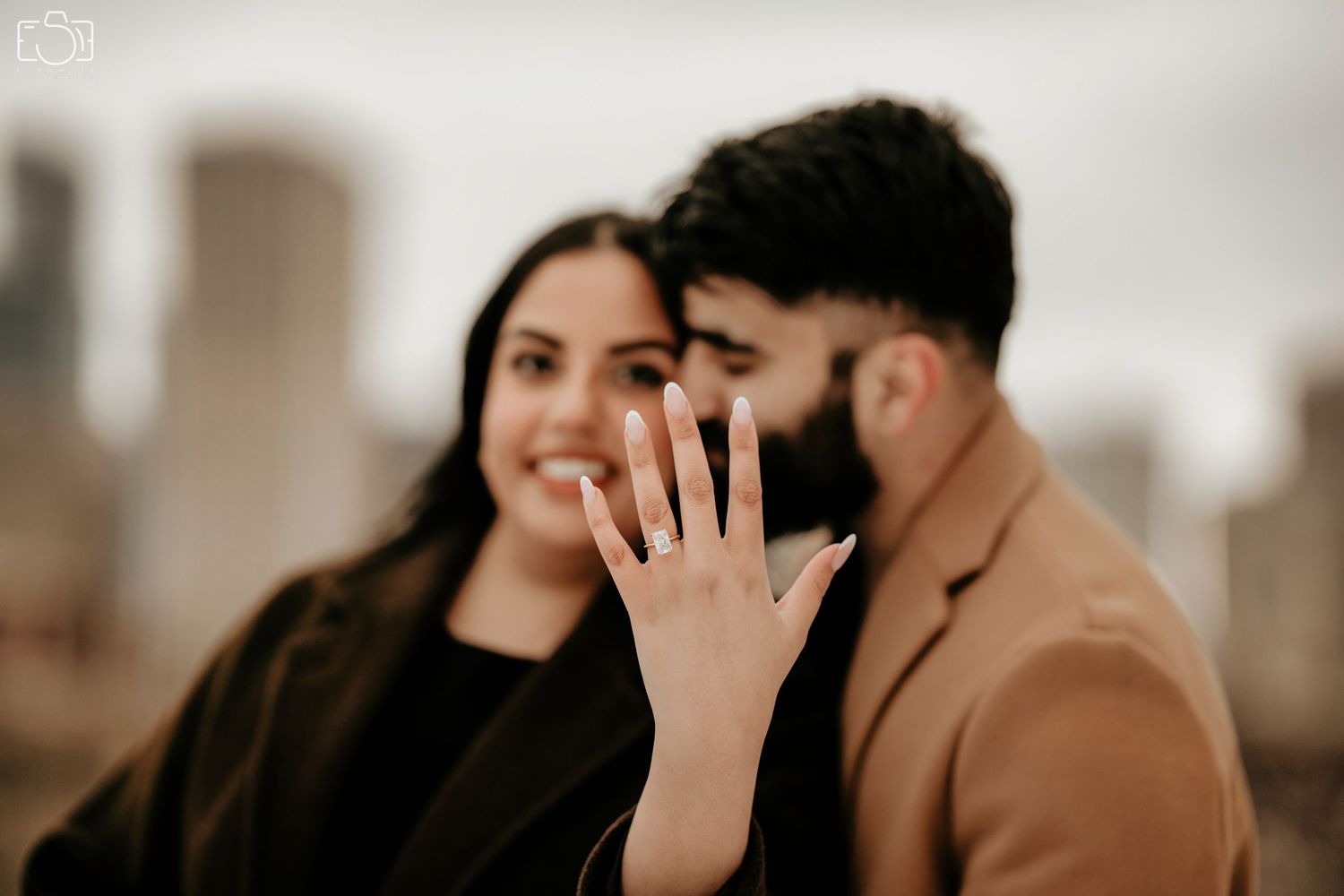 Happy couple showing off engagement ring against urban backdrop.