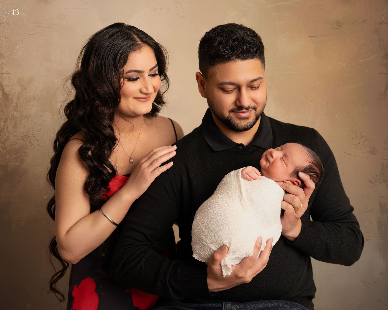 Family portrait with newborn baby against neutral brown background.