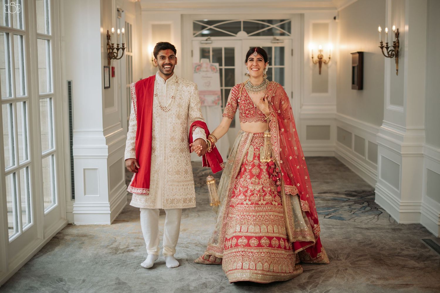 Traditional Indian wedding attire featuring red and cream colors in an elegant indoor setting.