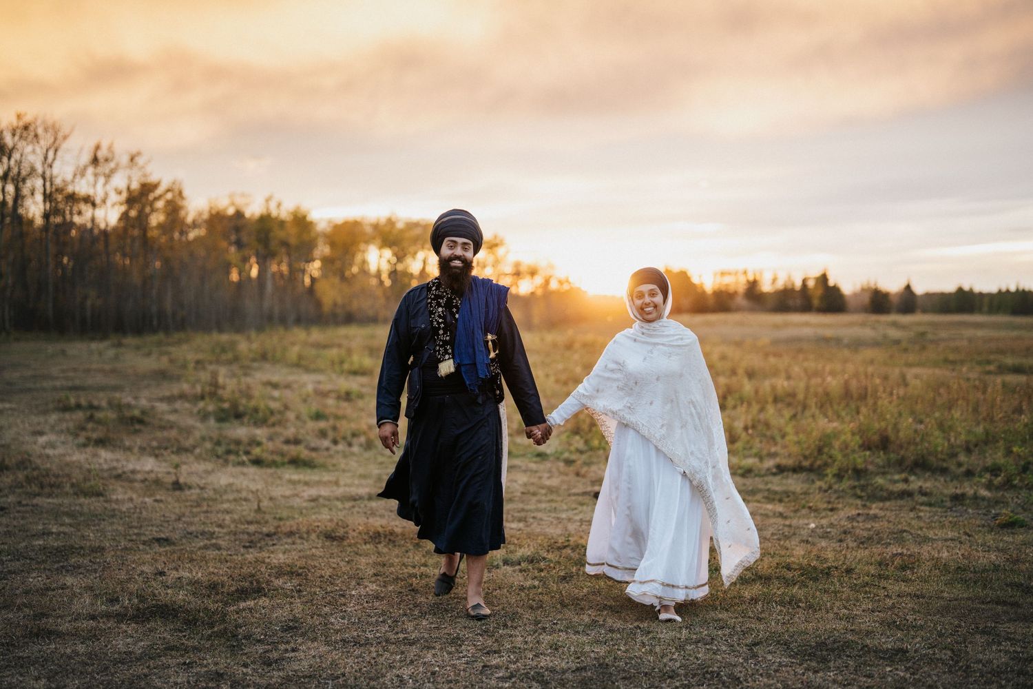 Two figures in flowing dresses walk through a golden autumn field at sunset creating a dreamy silhouette.