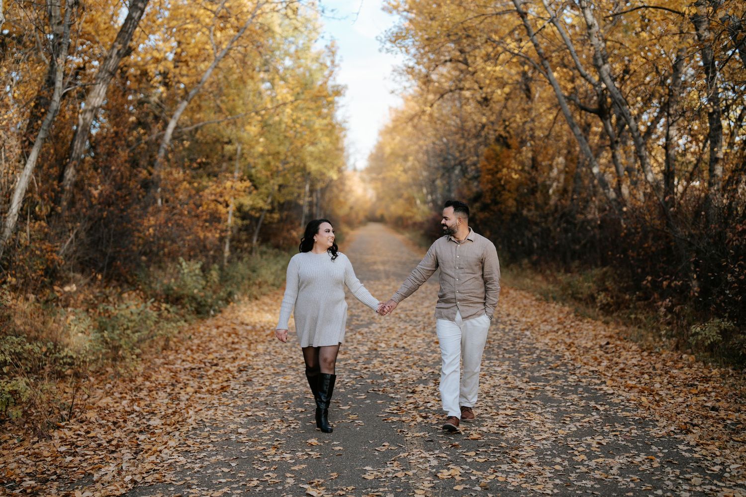 Couple holds hands while walking down leaf-covered path during autumn season.