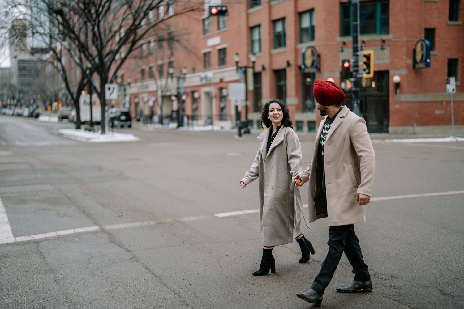 Couple walking through snowy urban street wearing winter coats.