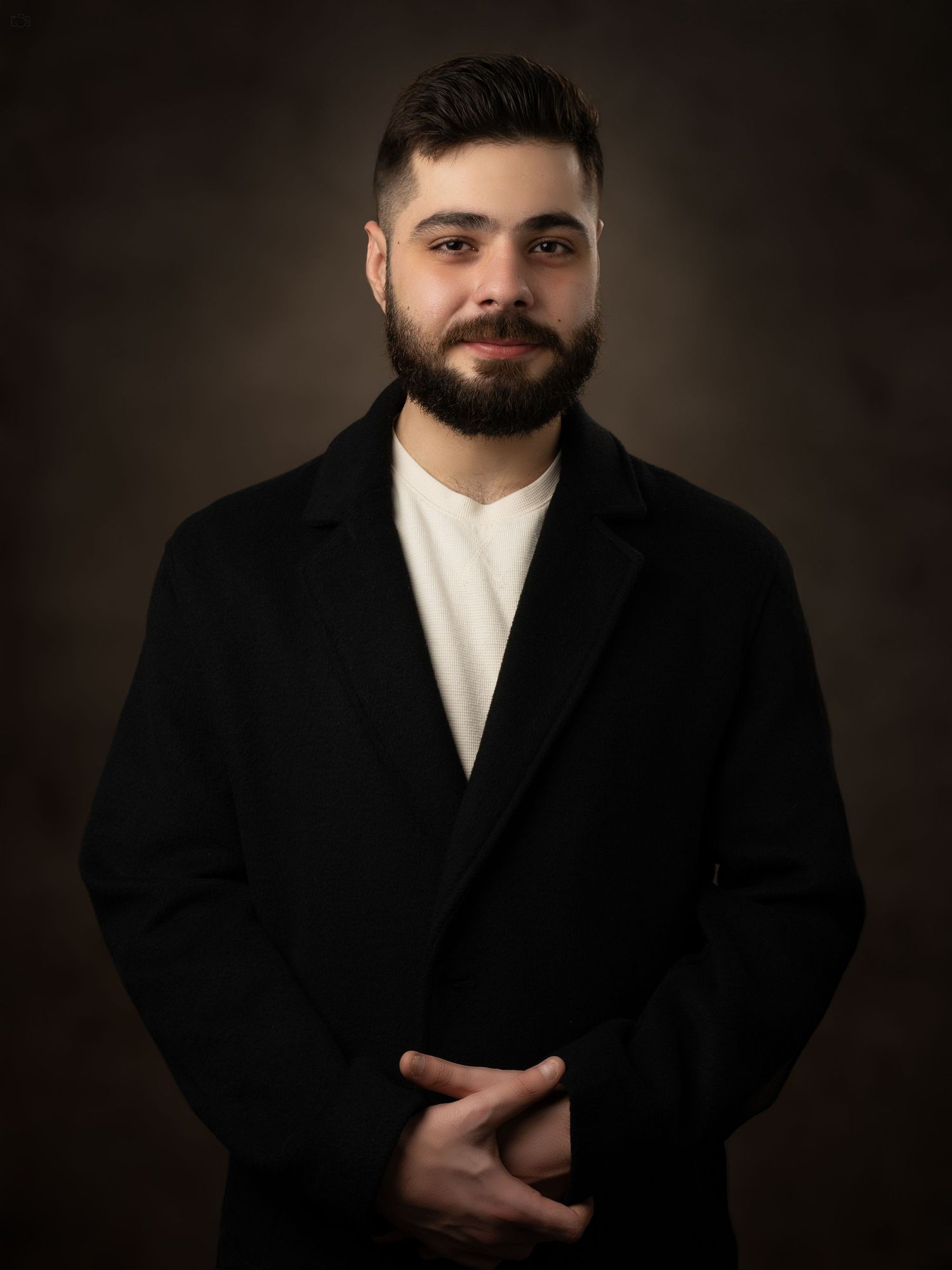 Professional headshot of a person wearing a black suit jacket and white shirt against a dark background.