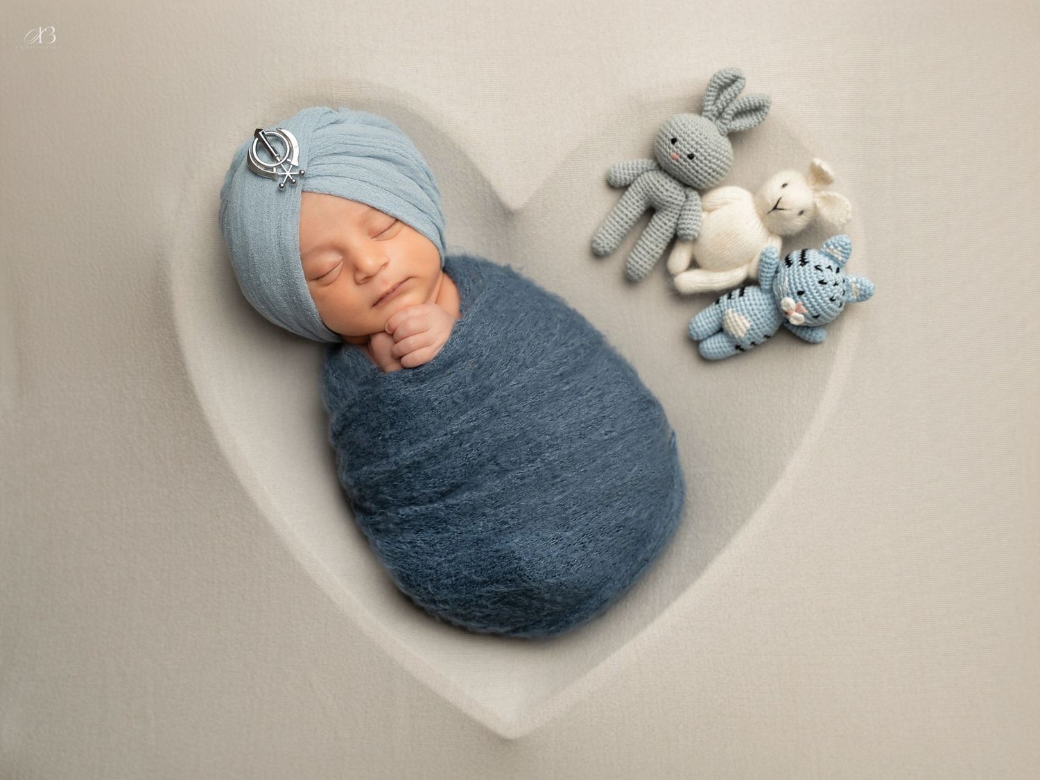 Newborn wrapped in blue swaddle sleeps peacefully in heart-shaped backdrop with plush toys.