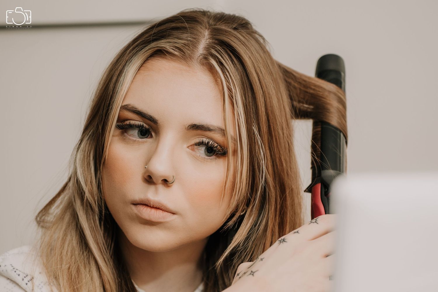 Woman styling her blonde hair with a curling iron while looking at herself in a mirror.