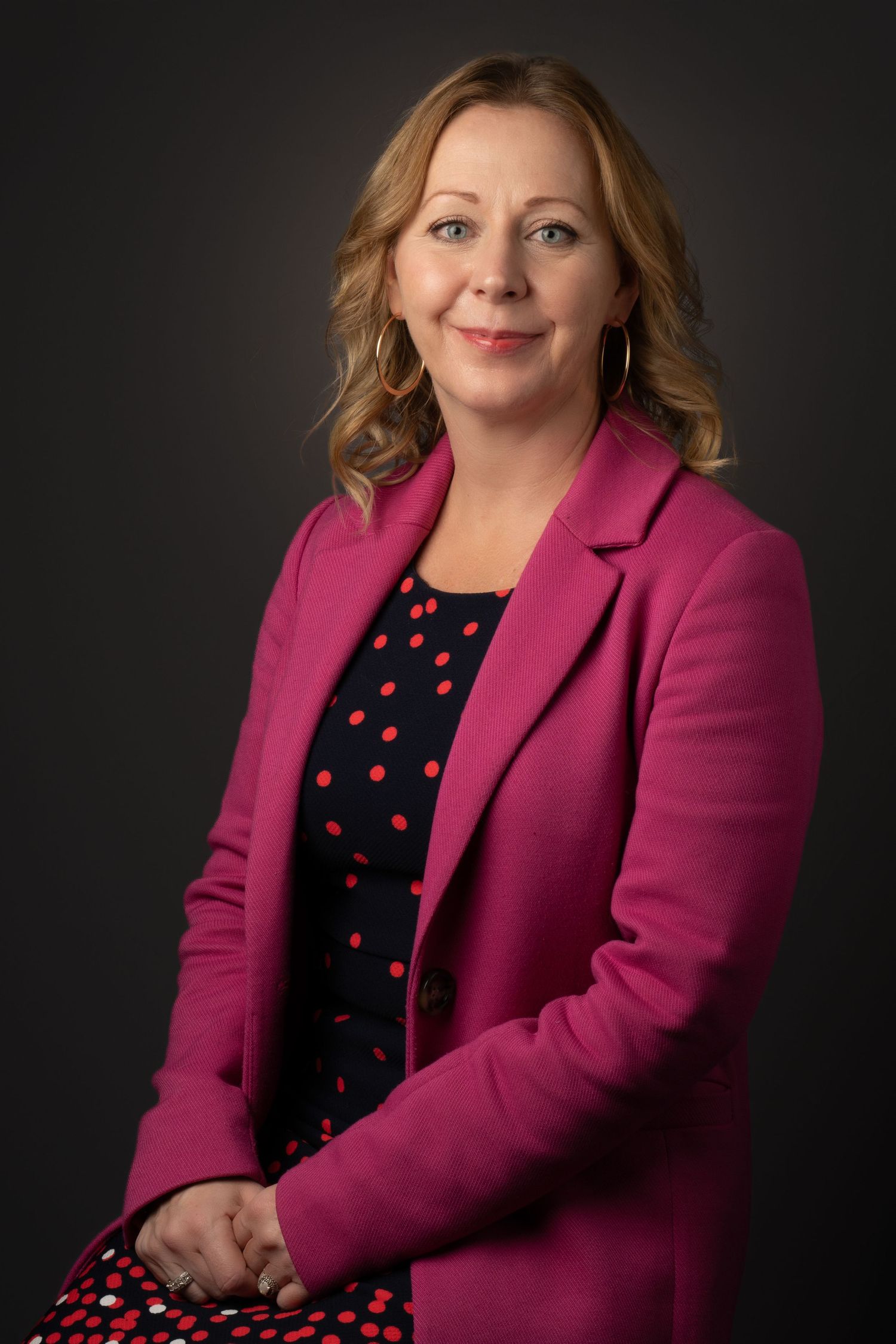 Professional portrait of a person in a bright pink blazer and polka dot dress.
