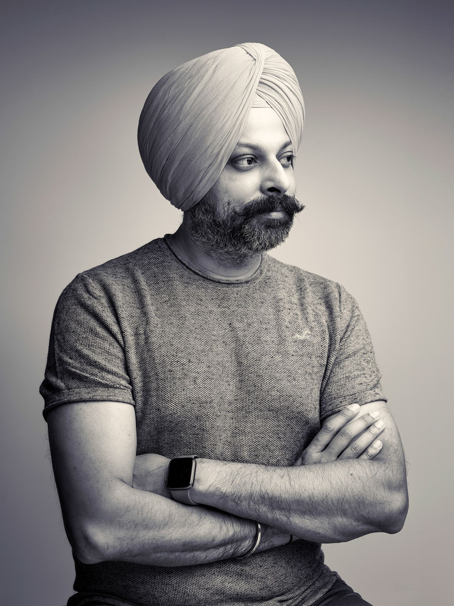 Portrait of man in turban and grey t-shirt with arms crossed against grey background.