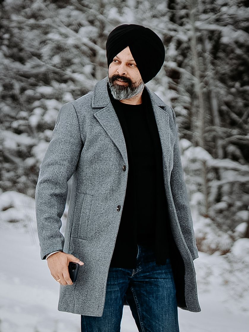 Winter portrait of person in grey coat and black turban against snowy forest background.