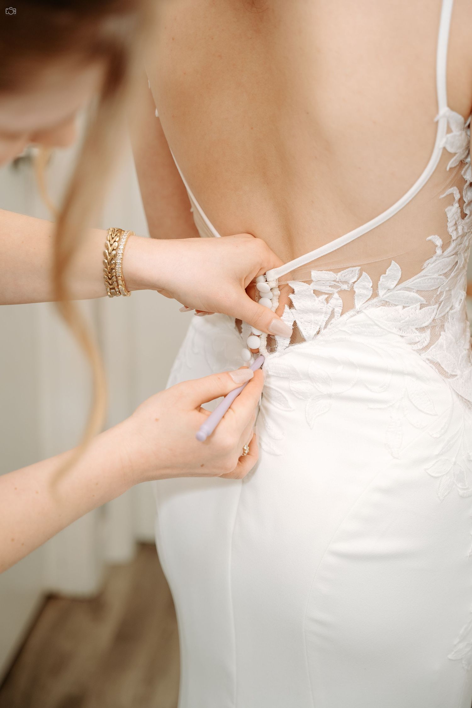 Close-up of delicate lace details being fastened on a white wedding dress.