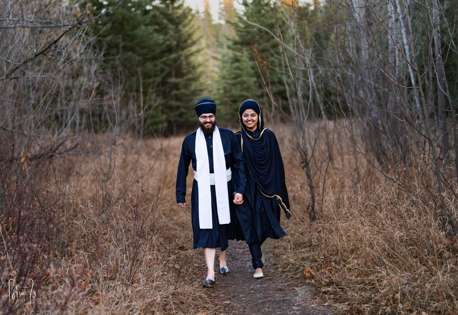 Two people walk together on a winding autumn forest path surrounded by bare trees and brown foliage.