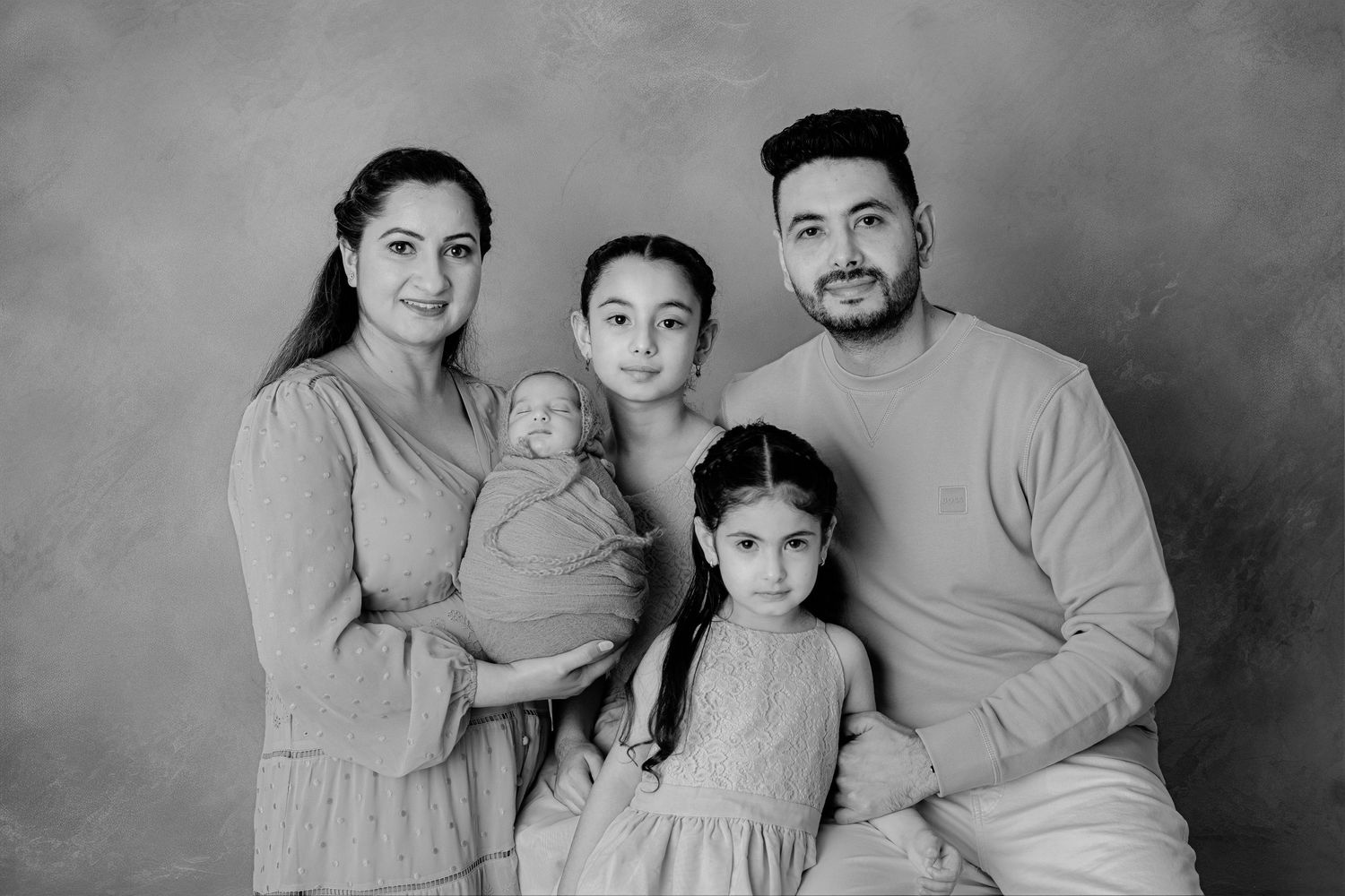A black and white studio portrait of a family of five in coordinating neutral colored outfits.